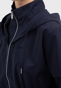 Navy blue lightweight jacket featuring a hood, silver zipper, and elastic drawstrings. Smooth texture with a relaxed fit and minimal detailing.