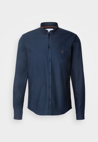 Mörkblå skjorta med knappar, långa ärmar, krage och orange accenttråd. Har en liten broderad detalj på bröstet.