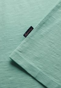 Jasnozielona tkanina o fakturze, z folded rękawem i małą granatową metką z różowym napisem "Superdry."