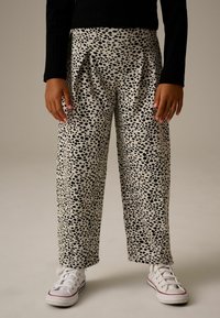 Pantalones de pierna ancha con estampado en blanco y negro, con pliegues, hechos de un tejido suave, que presentan un divertido diseño de lunares. Combinados con zapatillas blancas.