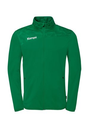 Veste de sport verte à fermeture éclair intégrale avec motif géométrique sur les épaules, col montant, poches latérales zippées et logo "Kempa" sur la poitrine gauche.