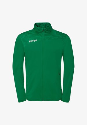 Veste de sport verte à fermeture éclair intégrale avec motif géométrique sur les épaules, col montant, poches latérales zippées et logo "Kempa" sur la poitrine gauche.