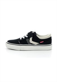 Zapatillas de lona negras con suela de goma blanca y cordones. Presentan una correa de Velcro y un elemento de diseño en beige a contraste en el costado.