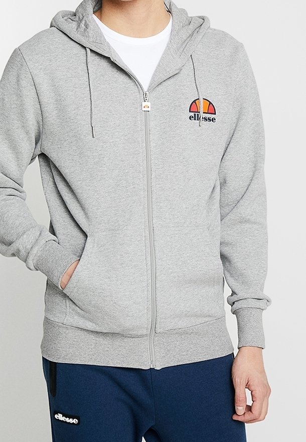 Felpa grigia chiara con zip in tessuto morbido, dotata di tasca a marsupio. Presenta un logo colorato Ellesse sul petto e un cappuccio con cordino.