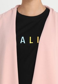 Avvolgente drappeggio rosa chiaro sopra una t-shirt nera. La t-shirt presenta lettere ricamate multicolori che formano la parola "ALI". Tessuto dalla texture liscia.