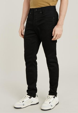 Black denim jeans with a slim fit, featuring front pockets and a button closure. Paired with white athletic sneakers.