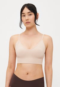 Vaaleanbeige ribbed bralette, jossa on V-muotoinen kaula-aukko, säädettävät olkaimet ja lyhyt muotoilu. Sujuva pinta ja minimalistinen tyyli.