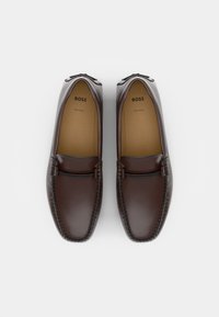 Mocassins en cuir marron avec des coutures et un petit accent métallique à l'avant. Les semelles intérieures sont de couleur beige, portant le nom de la marque "BOSS."