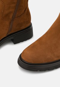 Ruske nubuck ankle boots s zaobljenim vrhom, teksturiranim gornjim dijelom, dekorativnim šavovima, bočnim patentnim zatvaračem i čvrstim crnim gumenim potplatom.