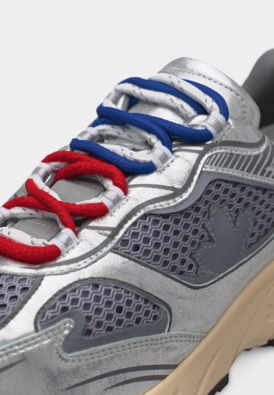 Ασημένιο και γκρι αθλητικό παπούτσι με πάνελ από δίχτυ και πολύχρωμα κορδόνια κόκκινου, λευκού και μπλε χρώματος, δεμένα χαλαρά στην κορυφή.