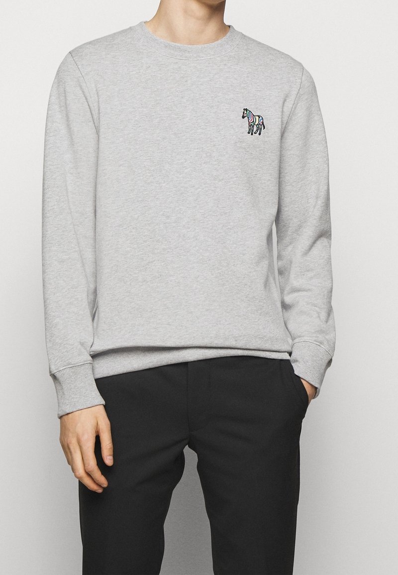 Sudadera gris hecha de una mezcla de algodón, con mangas largas, cuello redondo y un pequeño bordado de cebra colorido en el lado izquierdo del pecho.