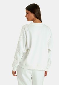 Maglione bianco con maniche lunghe, caratterizzato da ricami testurizzati lungo le cuciture delle spalle. Vestibilità rilassata, tessuto morbido e scollatura a costine.