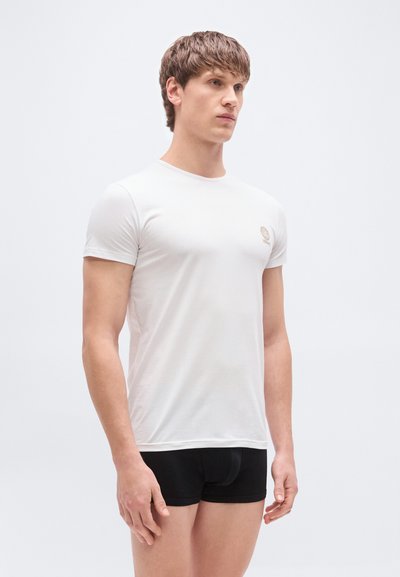 Λευκό εφαρμοστό T-shirt κατασκευασμένο από ελαφρύ ύφασμα, με στρογγυλή λαιμόκοψη και μικρό λογότυπο σε διακριτικό χρώμα στο στήθος.