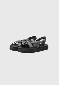 Sandali in pelle nera con design a tracolla incrociata, cinturino alla caviglia regolabile e suola spessa e testurizzata per il comfort.