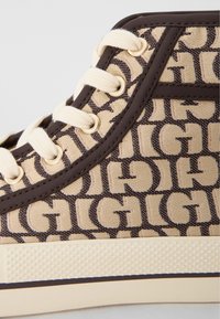 Hoge sneakers met een beige canvas bovenkant, voorzien van een donkerbruin logo patroon, crèmekleurige veters en een gestructureerde beige rubberen zool.