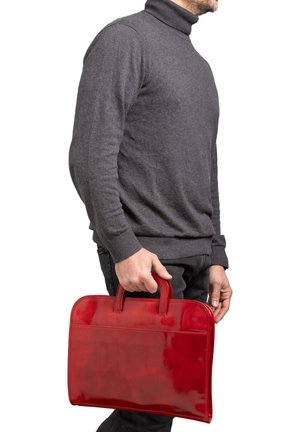 Man die een donkergrijze coltrui draagt en een felrode leren aktetas bij het bovenste handvat vasthoudt.
