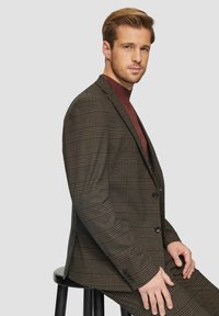Brązowy blazer w kratę, wykonany z teksturowanej tkaniny, z zapięciem na dwa guziki, klapami i delikatnymi niebieskimi akcentami w wzorze.