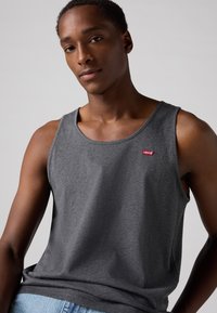 Débardeur gris sans manches en tissu doux avec un col rond et un petit logo rouge Levi's sur la poitrine. Texture lisse, coupe décontractée.