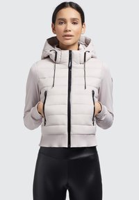 Hellgraue Daunenjacke mit Kapuze, ausgestattet mit schwarzen Reißverschlüssen, gerippten Bündchen und seitlichen Taschen. Glatter Stoff mit einem gesteppten Design.
