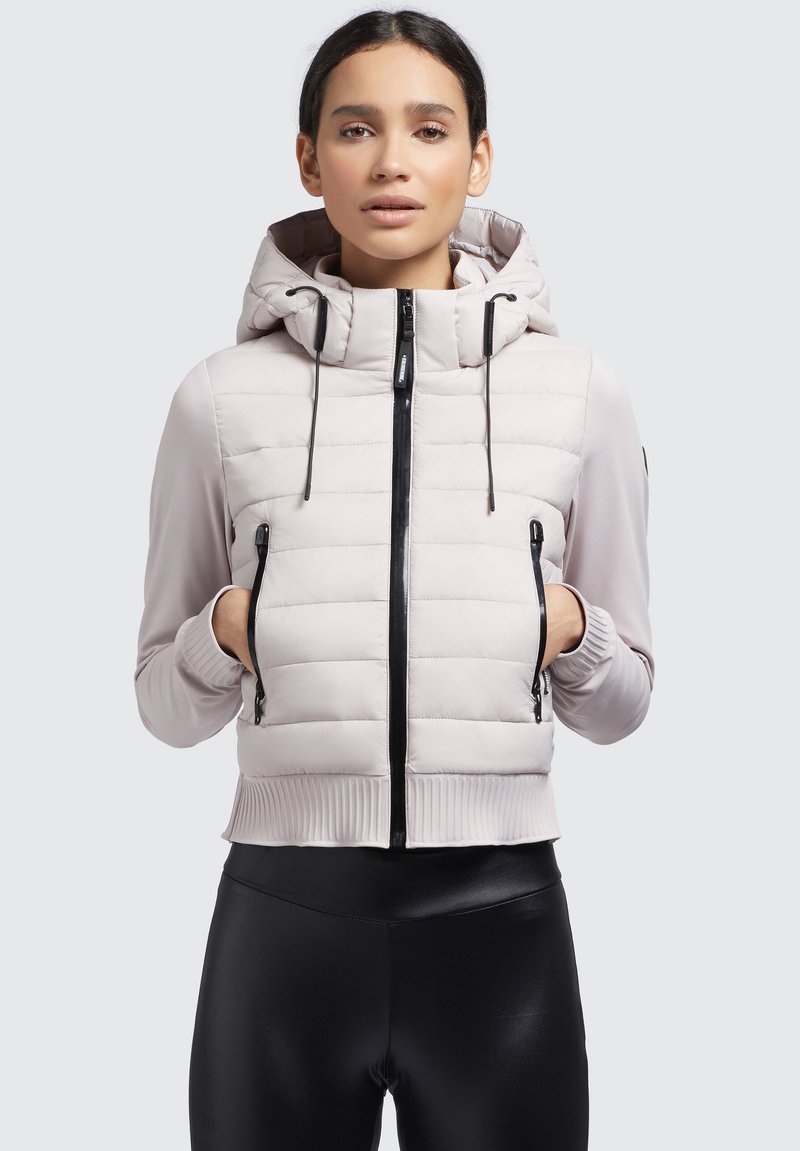 Hellgraue Daunenjacke mit Kapuze, ausgestattet mit schwarzen Reißverschlüssen, gerippten Bündchen und seitlichen Taschen. Glatter Stoff mit einem gesteppten Design.
