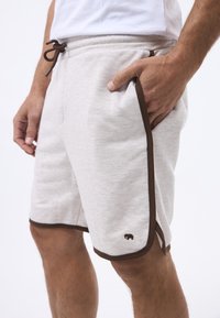 Shorts atletici grigi chiari con un cordino marrone e rifiniture a contrasto. Presentano tasche laterali e un piccolo logo di un elefante sull'orlo.