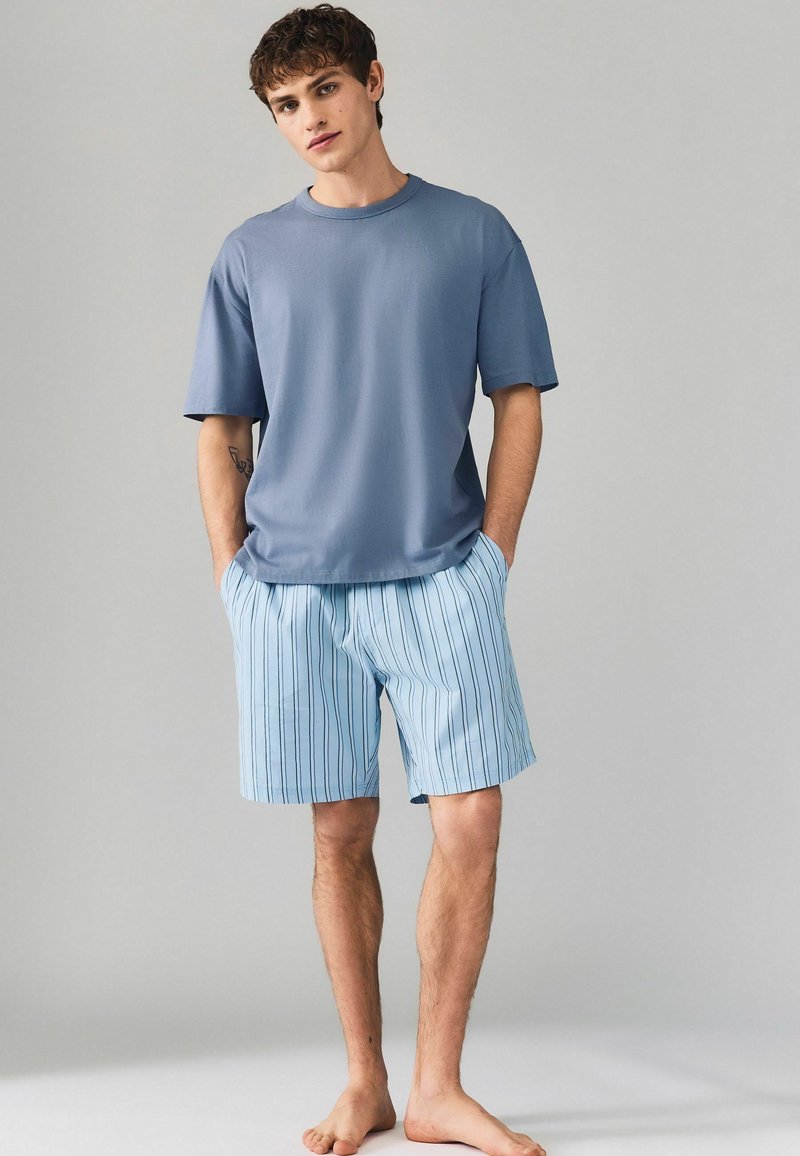 Kurzärmeliges blaues T-Shirt kombiniert mit hellblauen gestreiften Shorts, beide aus weichem, atmungsaktivem Stoff. Die Shorts haben vertikale Linien.