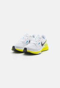 Baskets de course blanches avec une tige en mesh, logo Swoosh noir, semelle jaune vif et détails accentués en bleu sur les lacets et la languette.