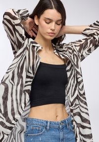 Blusa bianca trasparente con strisce zebra nere, indossata sopra un crop top nero a costine. Pantaloni shorts in denim blu a vita alta con leggeri segni di usura.