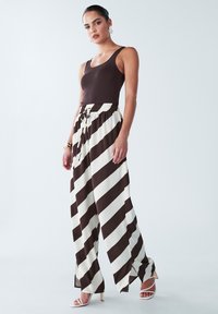 Brown ribbed tank top paired with wide-leg cream pants featuring bold brown stripes; relaxed fit with drawstring waist and side slits.