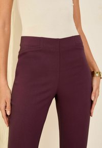 Pantalons bordeaux taille haute avec une texture lisse, dotés de poches latérales et d'une coupe ajustée. Accompagnés de détails de couture subtils.