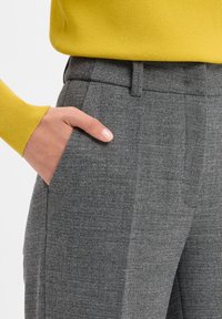GRAUE STRUKTURIERTE HOSE MIT EINEM MASSGESCHNEIDERTEN SCHNITT, MIT SEITENTASCHEN UND EINEM GLATTEN BUND. KOMBINIERT MIT EINEM HELLEN GELBEN STRICK-Oberteil.