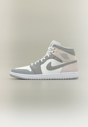 Harmaa ja valkoinen korkeavartinen lenkkari, jossa nauhat edessä ja Nike-swoosh-logo sivulla, esitetty yksinkertaisen neutraalin taustan edessä.