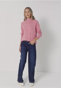 Rosa, langärmliger Pullover mit hohem Kragen; kombiniert mit dunkelblauen geraden Jeans und hellen Turnschuhen. Glatte Textur, lässiges Design.