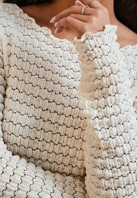 Gebreide trui in crèmekleur met een structuurpatroon. Heeft geschulpte manchetten en een ronde halslijn. Zacht fabric met open geweven details.