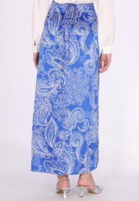 Blauwe maxi rok met een paisley patroon in het wit, gemaakt van gladde stof. Vetersluiting in de taille, met een ontspannen silhouet. Zilveren hakken zichtbaar.