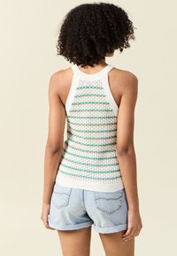 Gebreid tanktop met witte, groene en oranje horizontale strepen, met een geribde halslijn en zoom. Gecombineerd met lichtblauwe denim shorts.