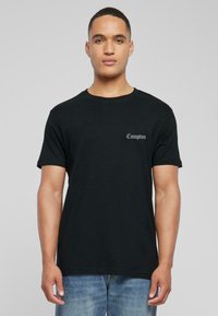 Camiseta de algodón negra con mangas cortas y cuello redondeado. "Compton" está impreso en una elegante tipografía en la zona izquierda del pecho.