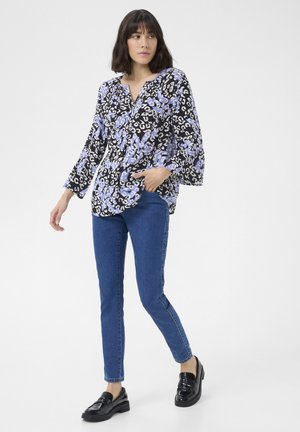 Blouse noire et lilas à motifs avec un col en V et des manches évasées, associée à un jean skinny bleu et des mocassins noirs plateforme.