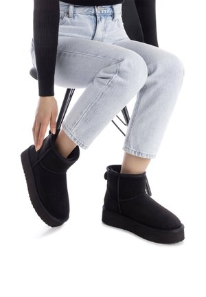 Stivaletti neri in suede con un morbido interno, punta tondeggiante e suola texturizzata; presentano un anello sul retro e cuciture curve decorative.