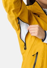 Gul vandtæt jakke med sorte lynlåse. Har en lynlåslomme på brystet og to sidelommer, lavet af glat, tekstureret stof.