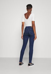 Body blanco de canalé con un profundo escote en la espalda, combinado con jeans ajustados de cintura alta en azul oscuro con costuras en contraste y bolsillos traseros.