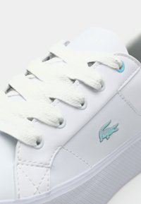 White sneaker with textured sole, flat white laces, and a turquoise Lacoste crocodile logo. Smooth synthetic material and minimal design.