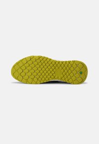 Semelle d'une chaussure avec un motif hexagonal, principalement en caoutchouc jaune, comprenant un logo circulaire et une surface texturée pour l'adhérence.