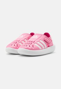 Sandalias slip-on Adidas de color rosa con rayas blancas y orificios de ventilación, que cuentan con suelas blancas acolchadas y correas ajustables en el talón.