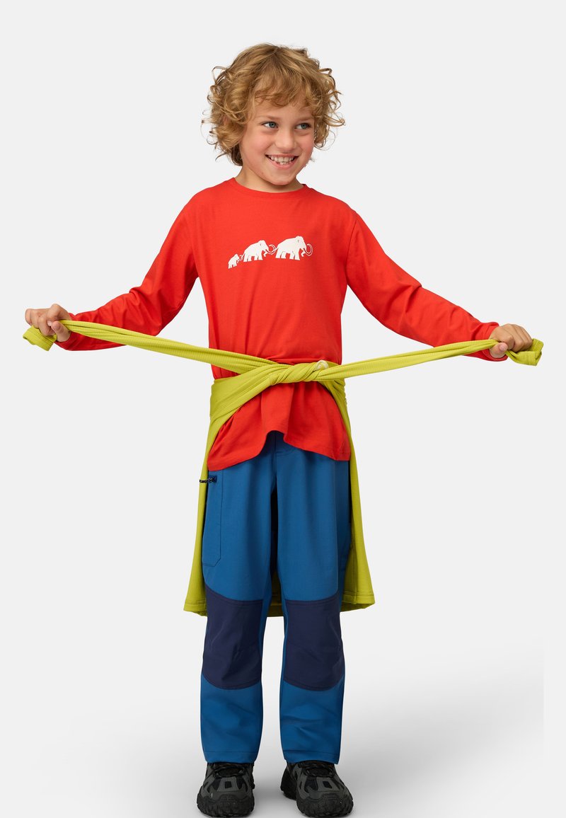 Rotes Langarmhemd mit weißem Elefantenmotiv, kombiniert mit blauen Hosen, die dunkelblaue Flecken aufweisen, und einem grünen Gürtel, der um die Taille gebunden ist.