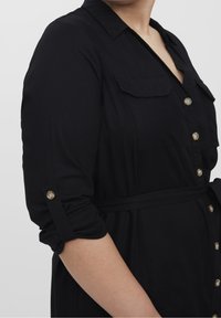 Czarna sukienka zapinana na guziki z kołnierzykiem, dwoma kieszeniami na piersi, podwiniętymi rękawami, materiałowym paskiem oraz złotymi guzikami z przodu.