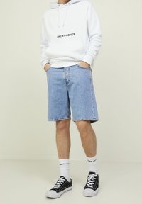 Ljusblå denimshorts, avslappnad passform, med synlig sömnad. I kombination med en vit hoodie med svart logotyp, svarta sneakers och vita strumpor.