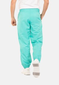 Turquoise sportbroek met een elastische tailleband, boorden en een gladde, lichte textuur. Draag met witte sneakers.
