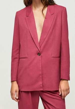 Donna che indossa un blazer rosa polvere su misura con un solo bottone e pantaloni coordinati, mostrata dalle spalle a metà coscia.