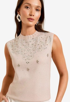 Pull sans manches rose clair avec un col en dentelle, orné de motifs en perles argentées et en sequins. Texture lisse, design ajusté.